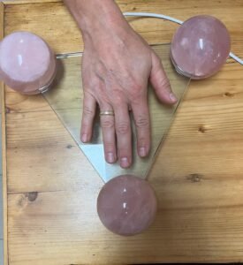Eine Hand liegt auf dem Radionik-Gerät mit Rosenquarz-Kugeln während einer energetischen Testung.