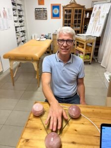 Ein Mann in einer Heilpraxis legt seine Hand auf das Radionik-Gerät mit Rosenquarzkugeln für eine energetische Analyse.