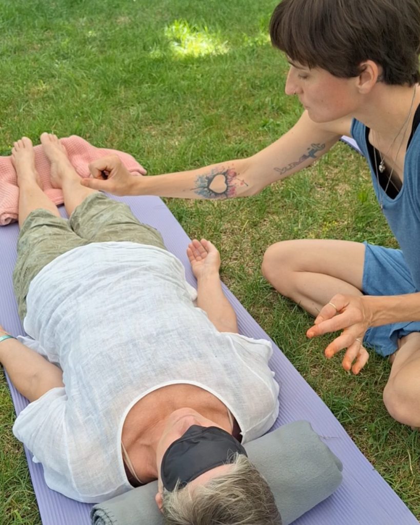 kundalini-activation-fortgeschrittene-session-im-freien Kundalini Activation Session im Freien – Karoline begleitet eine liegende Klientin mit sanften energetischen Impulsen an den Füßen